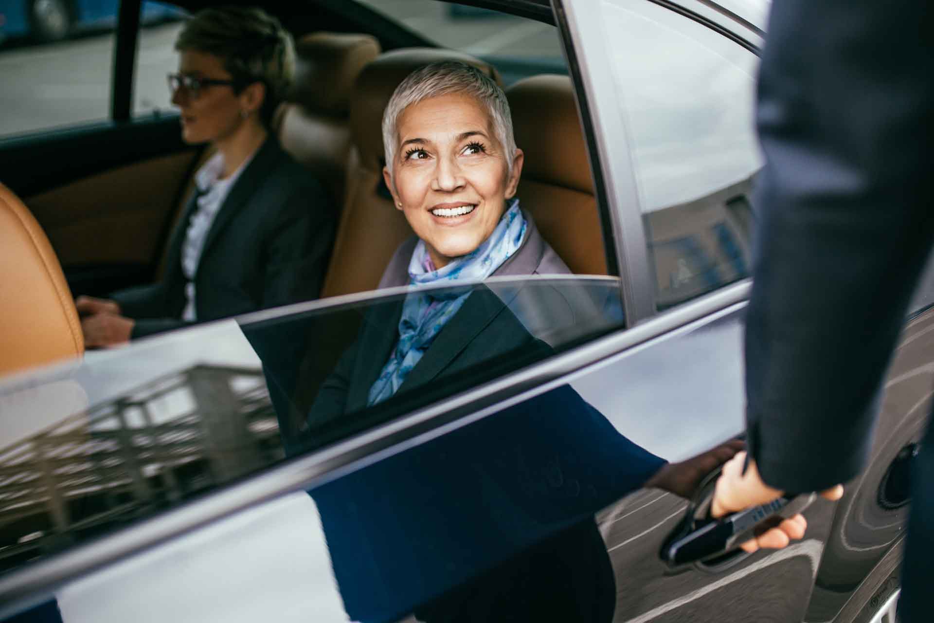 Business woman and assistant being let out of car by chauffeur